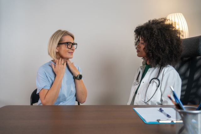 Untersuchung der Schilddrüsenfunktion. Freundliche junge afrikanische Ärztin untersucht Halsschmerzen oder Schilddrüsen. Männlicher Patient besucht Klinikbüro. Konzept zur Prävention von Schilddrüsenkrebs