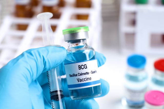 Das Foto zeigt eine Hand mit blauem Laborhandschuh, die ein Fläschchen mit dem BCG-Impfstoff sowie eine Spritze hält.