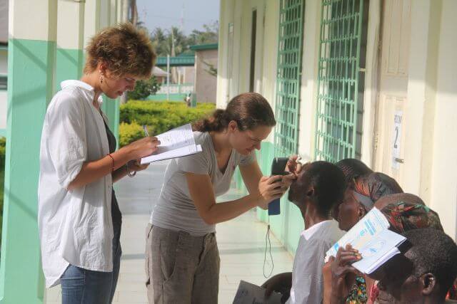 Junge Äugenärztin untersucht afrikanische Patienten auf einer Veranda