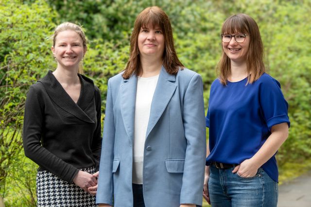 Drei Frauen stehen zusammen im Grünen und lächeln in die Kamera