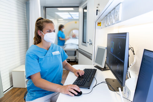 Krankenschwester arbeitet am Computer in einem Krankenhausraum mit Patienten im Hintergrund