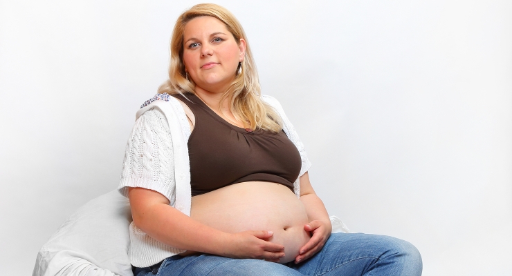 Symbolbild, übergewichtige schwangere Frau sitzt mit Händen auf Ihrem Bauch