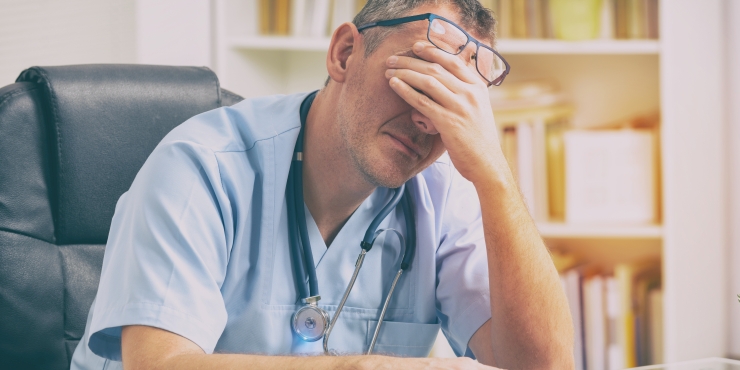 Symbolbild, überarbeiteter Arzt sitzt zusammengesunken am am Schreibtisch