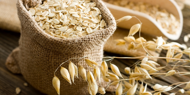 Symbolbild, Sack mit Haferflocken und einige frische Haferhalme im Vordergrund