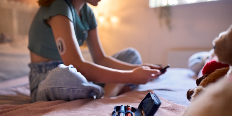 Symbolbild, Jugendliche mit CGM-Sensor sitzt auf dem Bett und schaut auf das Smartphone
