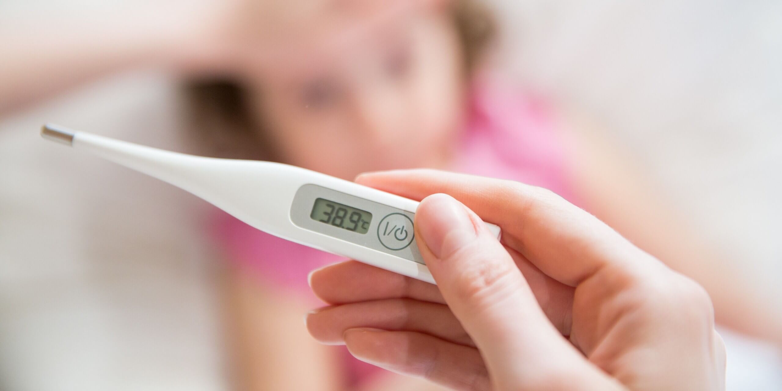 Kind mit Fieber liegt im Bett, Fieberthermometer zeigt 38,9 °C