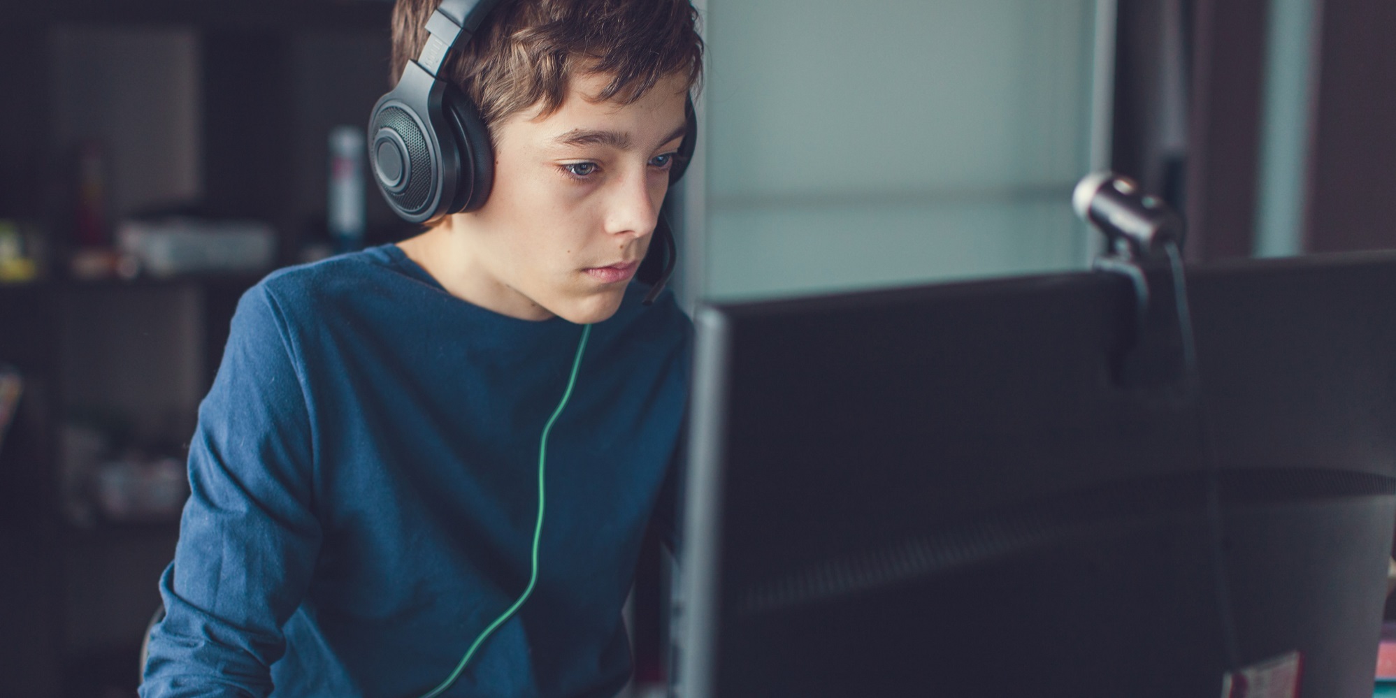 Jugendlicher sitzt mit Kopfhörern vor Computerbildschirm