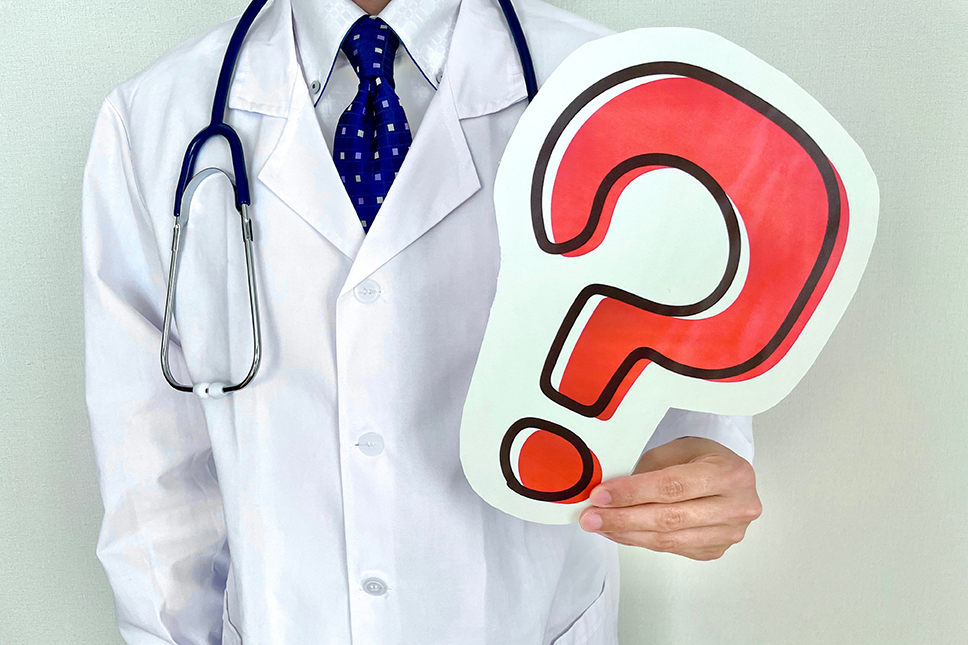 Ein Arzt im weißen Kittel mit Stethoskop hält ein großes rotes Fragezeichen in der Hand.
