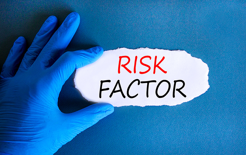 Hand in blauen Handschuhen hält ein Papier mit der Aufschrift „Risk Factor“ auf blauem Hintergrund.