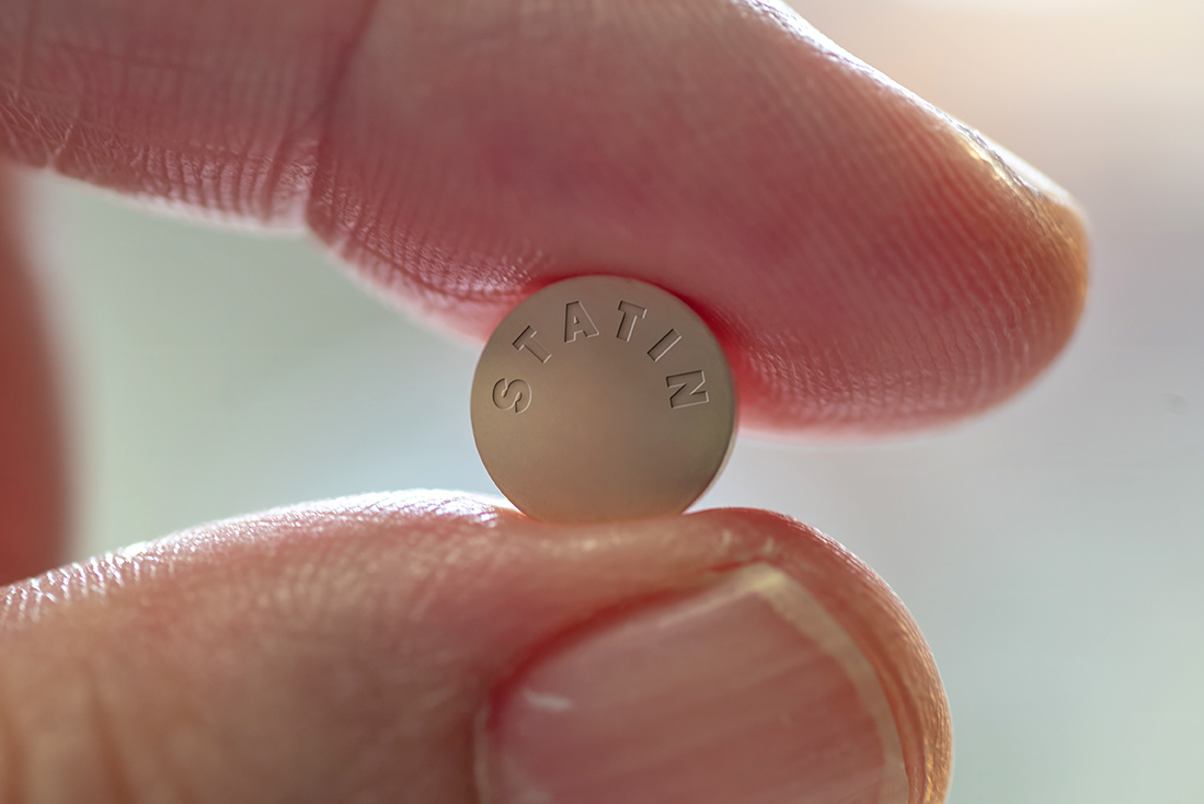 Nahaufnahme einer Statin-Tablette zwischen zwei Fingern, verwendet zur Senkung des Cholesterinspiegels.