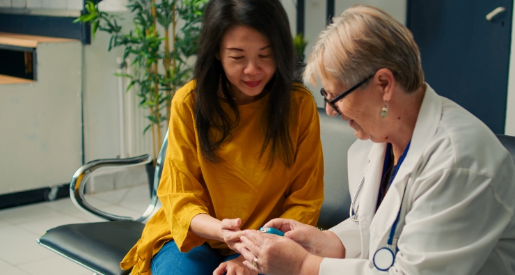Asiatische Frau bekommt von einer Ärztin am Finder den Blutzucker gemessen