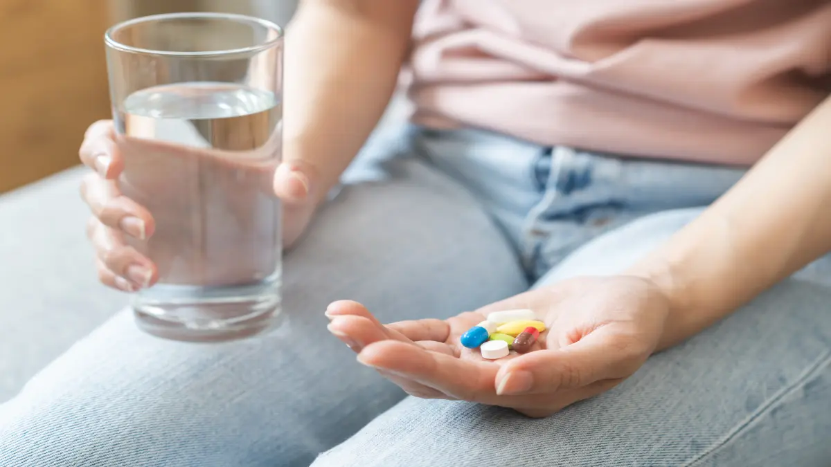 Junge Frau hält mehrere verschiedene orale Medikamente in einer Hand in der anderen ein Glas Wasser. Dies soll die Einnahme von Tumortherapeutika symbolisieren.
