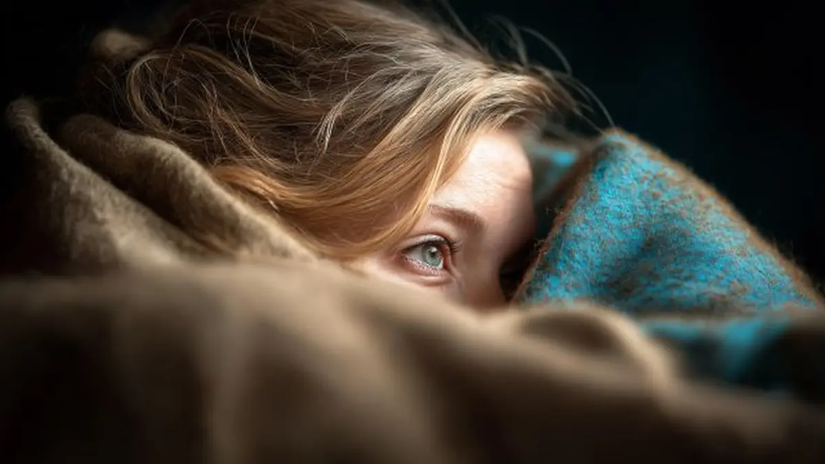 Eine Person liegt unter einer Decke in einem dunklen Raum, symbolisch für Depression und Rückzug.