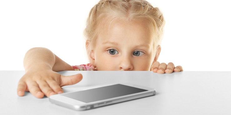 Kleines Mädchen versucht, Smartphone auf Tisch zu erreichen.