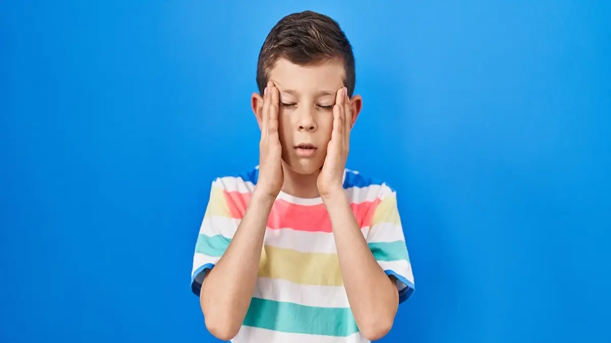 Junge mit Migräne hält seine Hände an die Schläfen