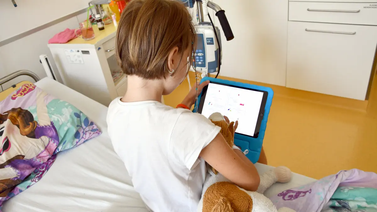 Kind tippt auf Tablet und sitzt am Krankenhausbett