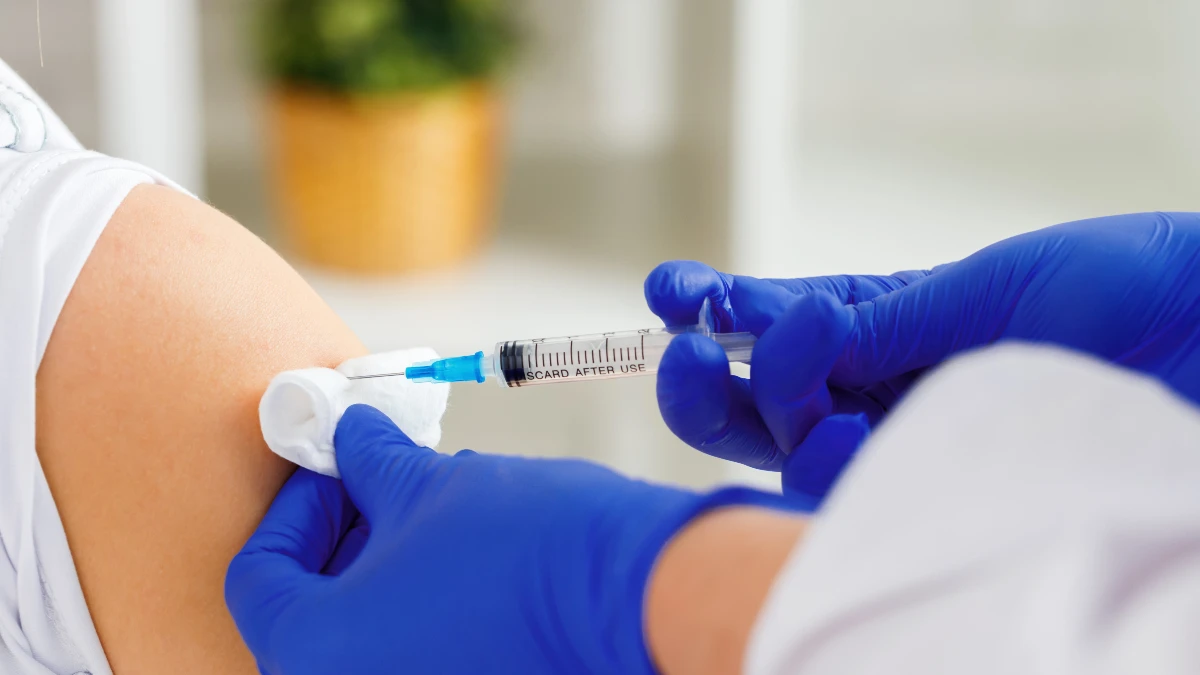 Darstellung einer Impfung: Ein Arzt hält eine Impfspritze an den Oberarm eines Patienten.