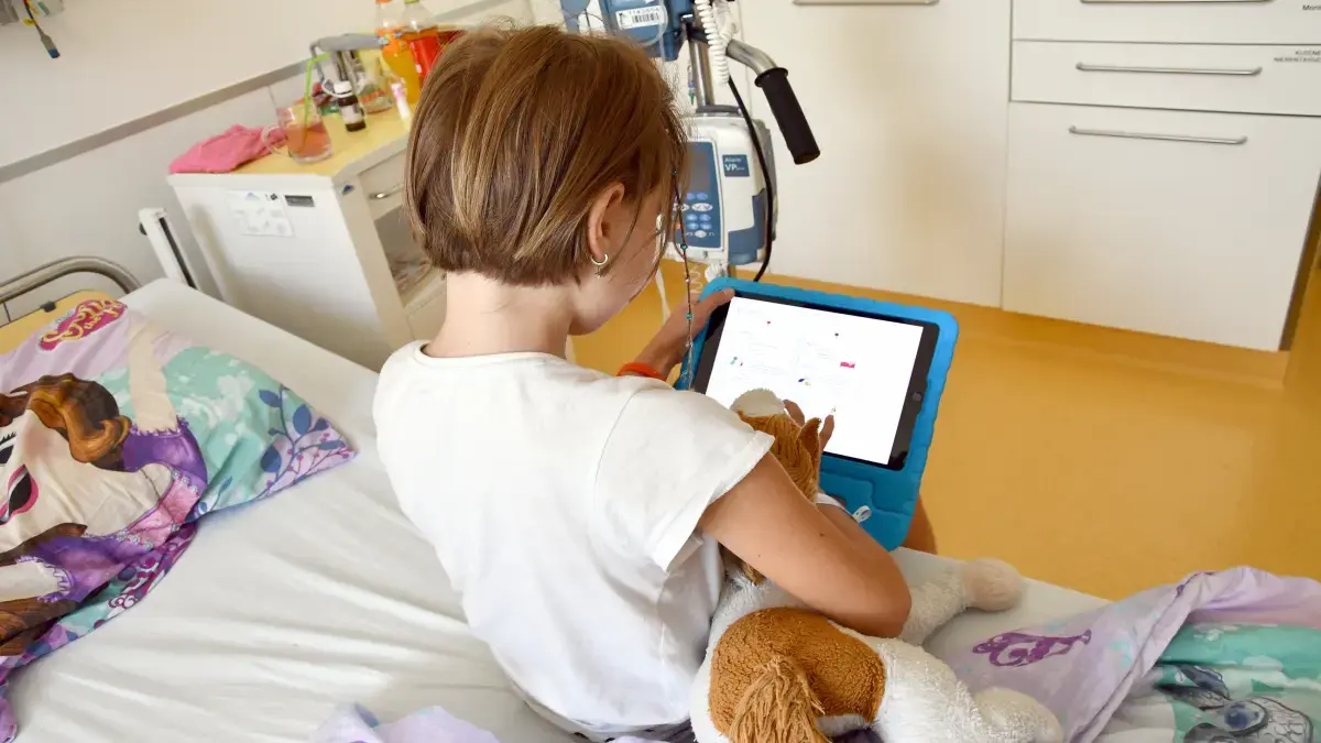 Kind übermittelt Symptome via App auf Tablet während der Krebsbehandlung