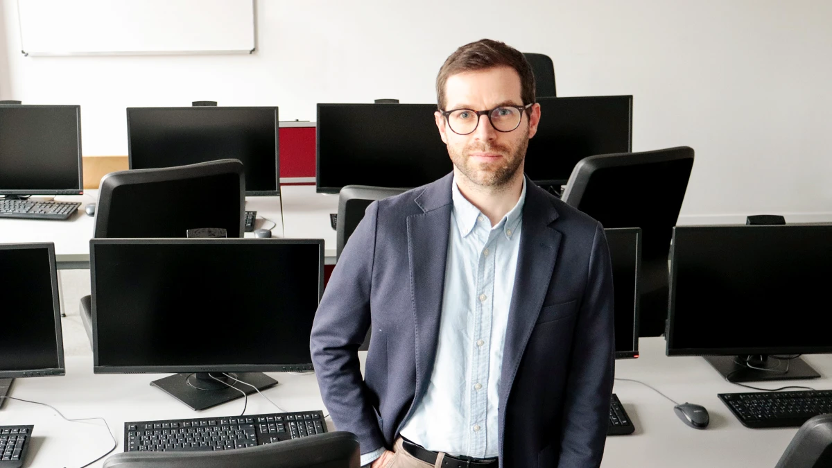 Prof. Dr. Marc Augustin steht im Computerraum und schaut in die Kamera