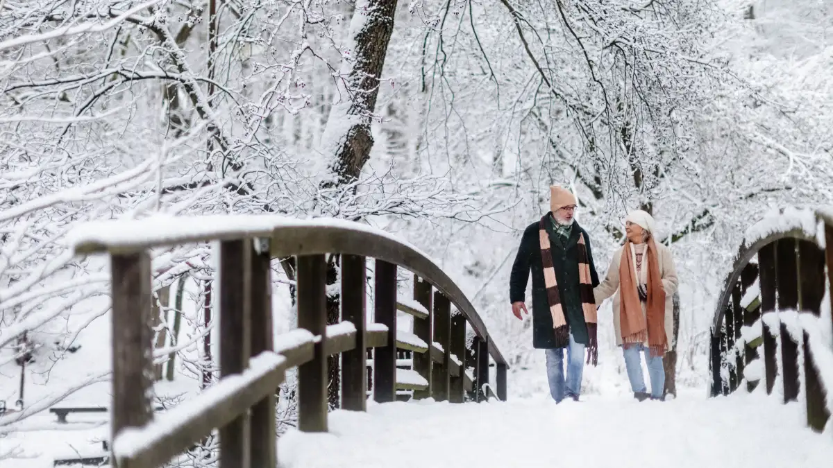 älteres Ehepaar gehen im Winter über eine schneebedeckte Brücke